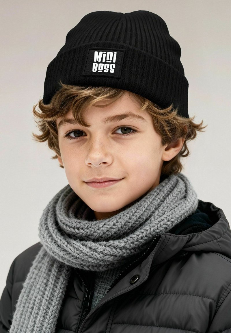 Black ribbed knit beanie with a white "Mini Boss" label, paired with a thick gray knitted scarf and a black puffer jacket.