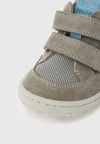 Chaussure en daim gris avec panneau en maille, deux brides à velcro, et semelle en caoutchouc gris clair. Comprend un col rembourré et un accent bleu sur la languette.