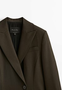 Blazer marron sur mesure avec un revers cranté, une fermeture à un bouton et une poche poitrine. Confectionné en tissu lisse, il présente un design minimaliste.