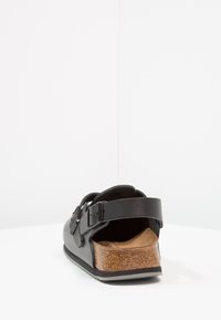 Sandalo nero con due cinghie regolabili, una soletta in sughero sagomata e suola in gomma nera testurizzata. Caratterizzato da una finitura liscia e da dettagli notevoli con fibbie.