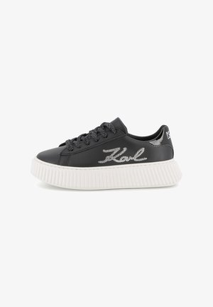 Baskets noires en simili cuir avec semelle en caoutchouc blanc texturé, lacets argentés et détail de logo brodé sur le côté.