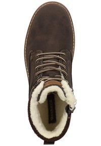 Brun snørebåndsstøvle med en tekstureret læderoverflade, hvid pelsfôr og tan detaljer. Har robuste brune snørebånd og syninger.