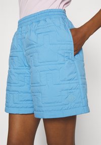 Light blue quilted shorts with an elastic waistband, side pockets, and geometric pattern texture. Features a small logo on the side.