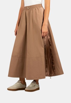 Gonna marrone, leggera, lunghezza caviglia con vita elastica arricciata, foderatura in satin e apertura laterale. Indossata con sneakers beige.