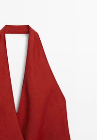 Red sleeveless dress with a deep V-neckline, made from textured fabric. Simple, long draping design with a broad neck strap.