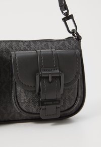 Black crossbody bag made of textured leather with a flap closure and metal accents. Features logo on hardware and smooth strap attachment.
