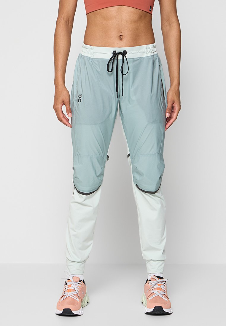 Leichte Jogginghosen in Mintgrün und Weiß, mit einem Kordelzugbund, Reißverschlusstaschen und kontrastierenden schwarzen Akzenten.