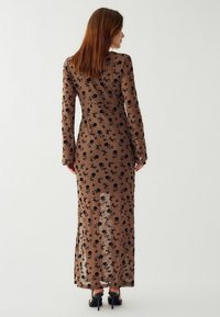 Dlhé, priliehavé šaty z priesvitnej hnedej látky s čiernymi kvetinovými vzormi. Majú dlhé rukávy a priame lemy, skombinované s čiernymi podpätkami.