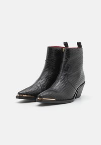 Botines negros de cuero con textura de piel de serpiente, con punta afilada, acentos dorados en la punta y un tacón bajo en ángulo.