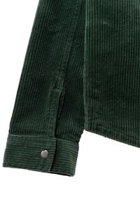 Tessuto di corduroy verde con righe verticali; presenta un dettaglio con polsini abbottonati. Texture morbida con un colore ricco e scuro.