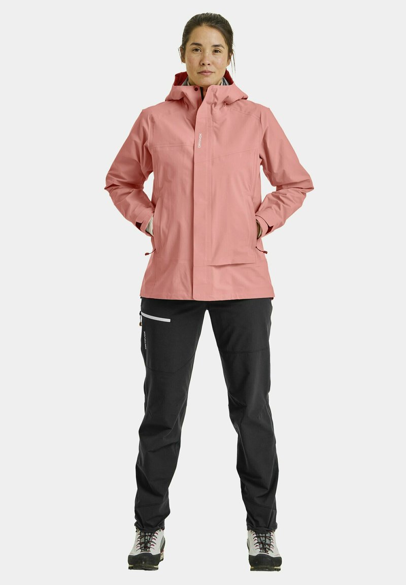 Light pink waterproof jacket with a hood, featuring a full front zip and side pockets. Paired with black pants with contrasting zippers.