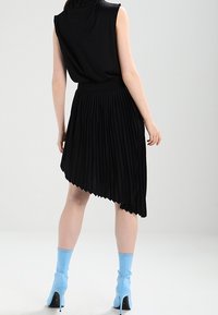 Top sin mangas negro combinado con una falda asimétrica plisada negra. El conjunto se complementa con unas botas de tacón alto azul hasta el tobillo.