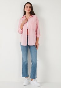 Light pink and white striped shirt with a classic collar, paired with blue flared jeans and white sneakers. The shirt features button closure and pocket.