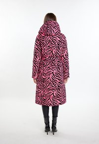 Długi płaszcz w różowym kolorze z czarnymi paskami w zebrę, z wysokim kołnierzem, paskiem w talii i długimi rękawami, w połączeniu z czarnymi botkami na obcasie.