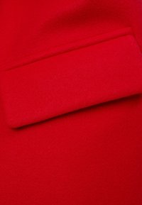 Röd ulltyg med en mjuk textur och ett ficklock, som visar en slät, jämn yta och en enhetlig färg.
