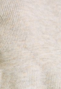 Gros plan sur un tissu tricoté côtelé de couleur crème douce avec une texture fine et des variations subtiles de couleur.