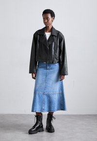 Veste en cuir noir courte, chemise blanche, jupe en denim bleu clair fluide, et bottines noires à lacets avec semelles épaisses.