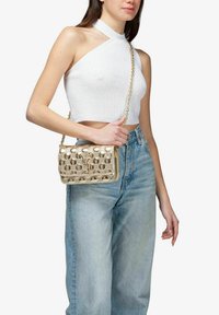 Borsa a tracolla in metallo dorato con un motivo circolare testurizzato, dotata di una tracolla a catena e chiusura a pattina. Indossata a tracolla con un abbigliamento casual.