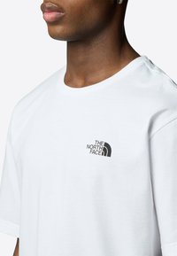 Hvid kortærmet t-shirt lavet af bomuld, med et sort broderet logo på venstre bryst. Rund halsudskæring med en afslappet pasform.