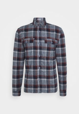 Camisa de franela a cuadros en gris, azul marino y burdeos con mangas largas, botonadura frontal y dos bolsillos en el pecho. Textura suave con cuello estándar.