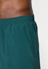 Calções atléticos em azul petróleo com cintura elástica; tecido leve; apresenta bolsos laterais e textura suave, destacando costuras limpas.