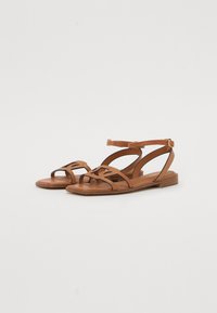 Sandales en cuir marron avec plusieurs lanières et une lanière de cheville, présentant une semelle plate en bois et des découpes pour la respirabilité.