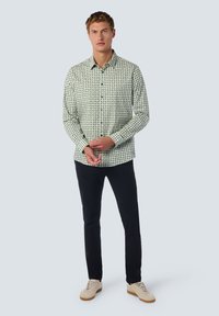 Een overhemd met knopen in een groen en zwart geometrisch patroon, lange mouwen en een kraag, gecombineerd met donkere broek en lichte sneakers.