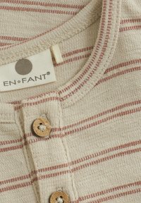 Beige randskjorta med tunna röda ränder, med rund hals, träknappstängning och mjuk texturerad tyg. Varumärkesetikett synlig.