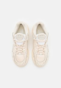 Zapatillas adidas beige con parte superior de malla y sintética, cuello acolchado, cordones planos y suelas texturizadas; cuenta con el logotipo en la lengüeta y el lateral.