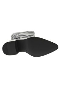 Semelle extérieure en caoutchouc noir d'une botte avec un motif de grip texturé, montrant un matériau supérieur gris élégant avec des détails froncés.