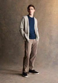 Light gray knitted cardigan over a navy t-shirt, paired with beige pants and black sneakers; features a relaxed fit and smooth texture.