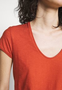 Rød bomulds T-shirt med korte ærmer og en dyb v-hals, der har en glat tekstur og en subtil melange mønster.