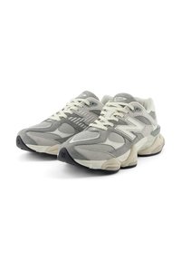 Ljusgrått sportskor med mesh- och mockamaterial, en vadderad krage, krämfärgade snören och en svart gummisula.