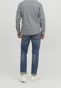 Camicia a quadratini bianca e nera, jeans in denim blu, sneakers bianche. La camicia ha maniche lunghe, polsini abbottonati e una vestibilità comoda. I jeans sono arrotolati ai polsini.