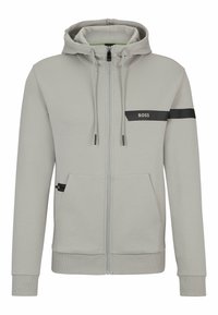 Ljusgrå zip-up hoodie med justerbar dragsko, svarta accentlinjer, framfickor och logotyp. Slät textur med ribbade mudd och fåll.