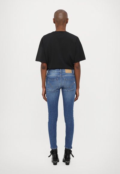 Svart kortermet t-skjorte, blå smale jeans med baklommer, og svarte ankelstøvler med dekorativ sløyfedetalj, sett fra bak.