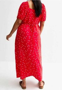 Rotes Maxikleid mit weißen Punkten, kurzen Puffärmeln, quadratischem Rücken und einem Taillengürtel. Glattes Material mit fließendem Design.