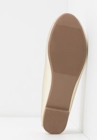 Beige kumikengäns, joka on varustettu teksturoidulla pidolla ja siinä on kohokuvioitu koko 37. Sileä, kerma värinen yläreuna, jonka muoto on hieman kaareva.