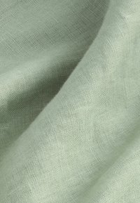 Tela de lino verde claro, con una fina textura y una superficie suave y lisa, exhibida en suaves pliegues.