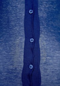 Marinblå knappad skjorta med en strukturerad, något genomskinlig tyg. Har en central knappslå med runda blå knappar och en volangkant.