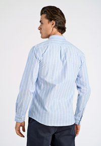 Camisa de manga larga azul claro con rayas verticales blancas, cuello con solapa, textura sutil y detalles de botones en los puños.