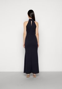 Vestido navy de cuello halter con apertura en la espalda y cuerpo ajustado, que fluye hacia un diseño de largo hasta el suelo. Presenta una tela suave y un detalle mínimo.