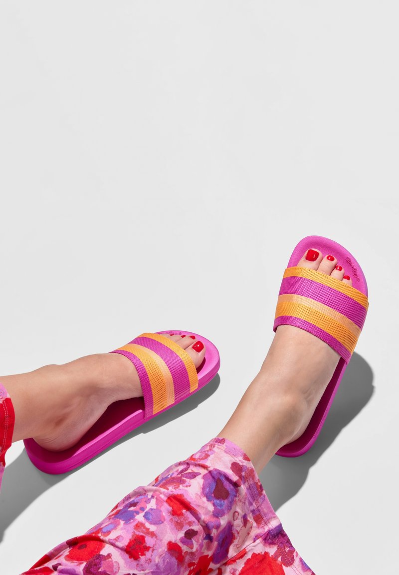 Pink and orange slide sandals with striped fabric upper, textured footbed, and a flat rubber sole, paired with floral patterned pants.
