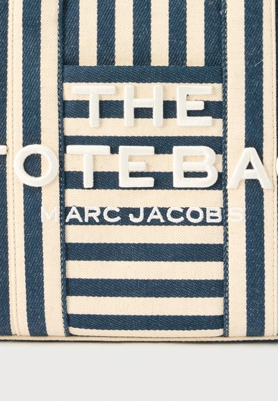 Ύφασμα με μπλε και μπεζ ρίγες με ανάγλυφα λευκά γράμματα που σχηματίζουν τη φράση «THE TOTE BAG» και μικρότερο κείμενο «MARC JACOBS» από κάτω.