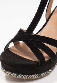 Czarne zamszowe sandały na platformie z krzyżującymi się paskami oraz plecioną juteową podeszwą. Cholewka ma miękką fakturę, a podeszwa charakteryzuje się teksturowanym wykończeniem.