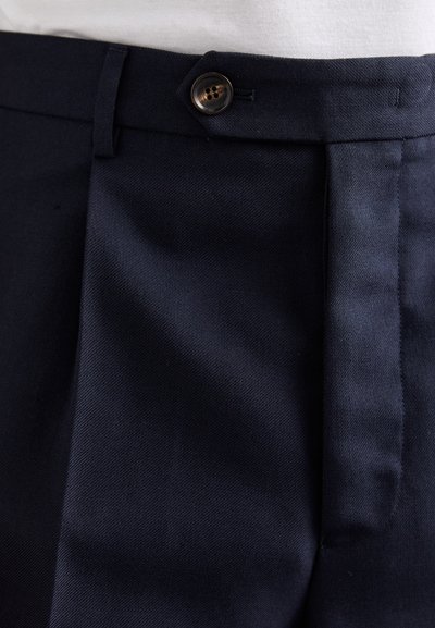 Pantalons bleu marine en matériau texturé ; dotés d'une fermeture à bouton visible et de plis avant pour un détail supplémentaire.