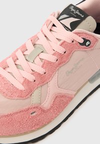 Roosa tossu, mis on valmistatud siledatest ja tekstureeritud materjalidest, omades heleroosasid paelu, beeži aktsenti ja musta logo sildikest.