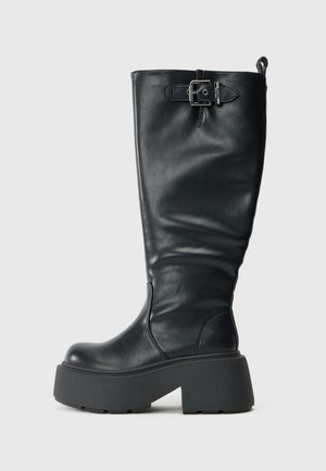 Μαύρη δερμάτινη μπότες μέχρι το γόνατο με χοντρή πλατφόρμα, διαθέτει φερμουάρ στο πλάι, ρυθμιζόμενο δέσιμο με μεταλλική αγκράφα και λεία υφή.