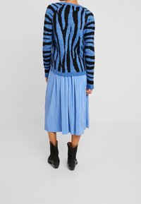 Blå stickad tröja med svarta tigerränder, i kombination med en veckad ljusblå kjol och svarta ankelstövlar. Strukturerad tyg och lagerdesign.