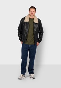 Černá kožená bunda s béžovým beránkovým límcem, zelené tričko, modré džíny a tenisky s jemně šedým a černým detailem.